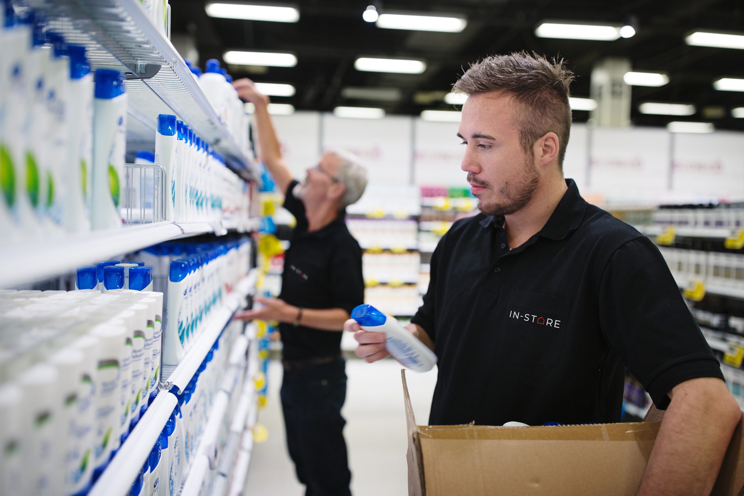 To IN-STORE merchere fylder varer op i personlig pleje-afdelingen.
